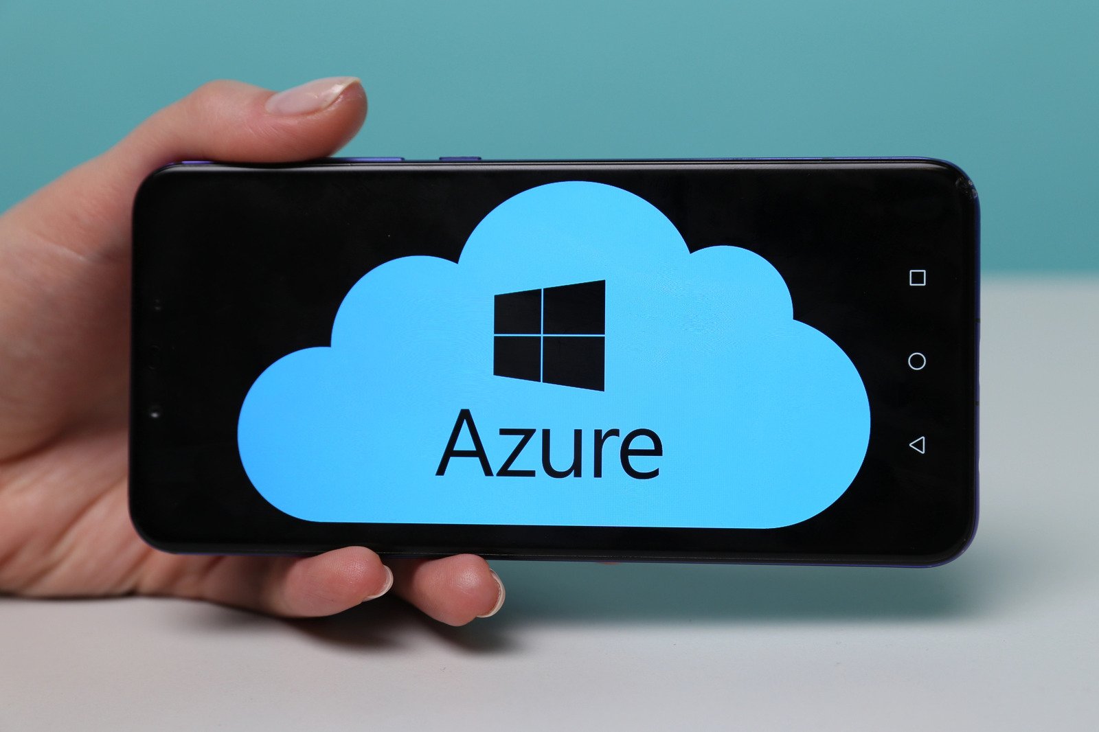 A smartphone displaying a blue cloud with the Windows logo and the words Microsoft Azure Cloud Services on the screen, held by a hand.