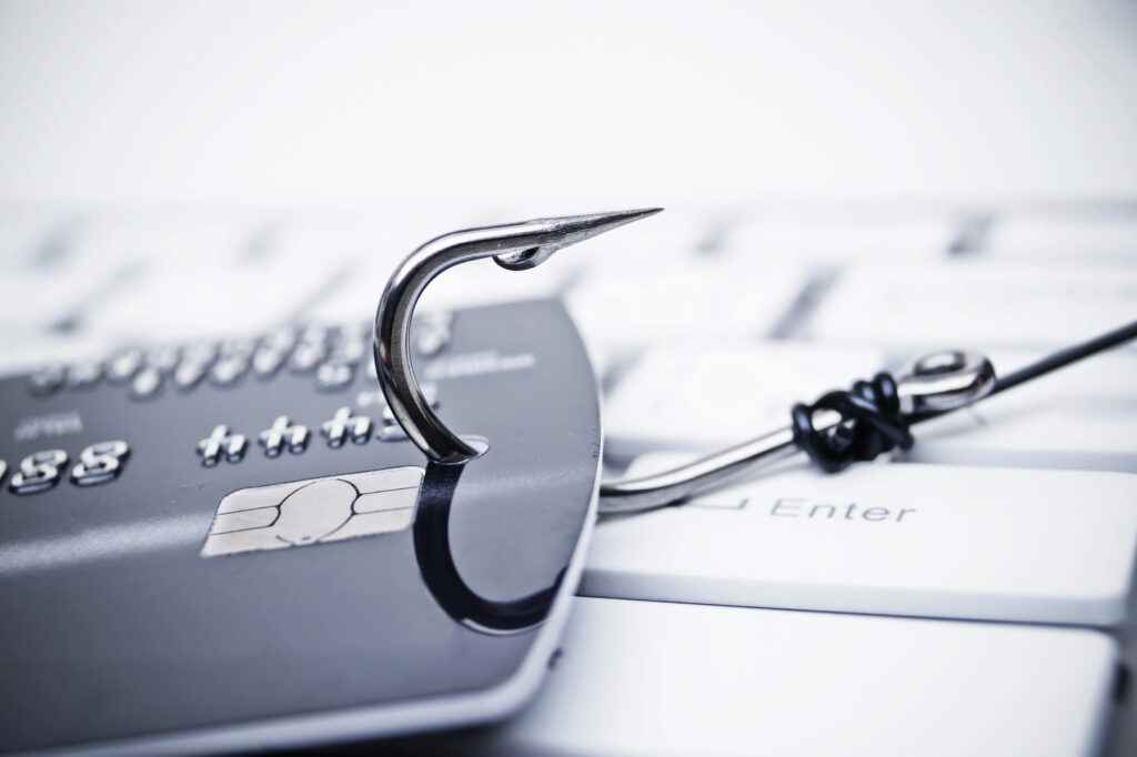 A credit card, pierced by a fish hook, lies on a computer keyboard, vividly symbolizing phishing or online financial threats in the realm of cyber security.